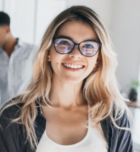 Smiling woman with blue-rimmed glasses in a bright office setting