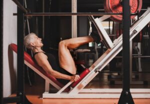 Older woman performing a leg press on a red-and-white weight machine in a gym.
