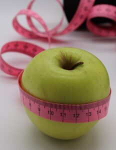 Green apple with a pink measuring tape wrapped around it, signaling dieting or healthy eating.