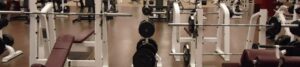 Row of squat racks and benches with barbells and weight plates in a spacious gym area