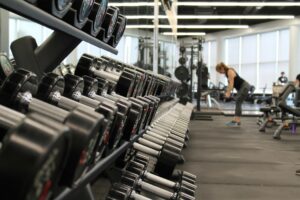Dumbbell rack in a gym foreground with people exercising blurred in the background.
